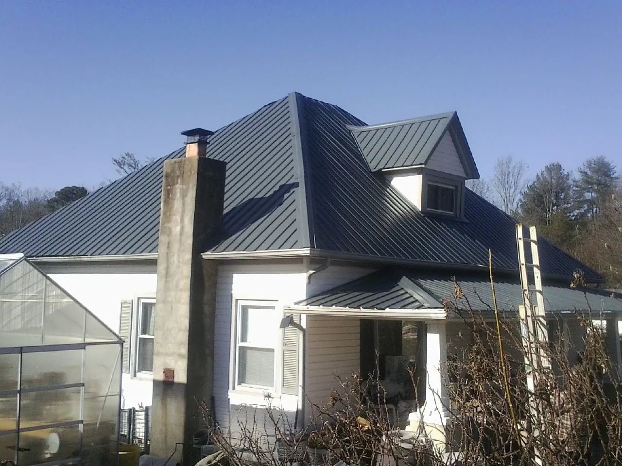 Dark blue standing seam metal roof on a white farmhouse with dormer — Slate & Tile Roof Repair by Roofing Brothers in Wake