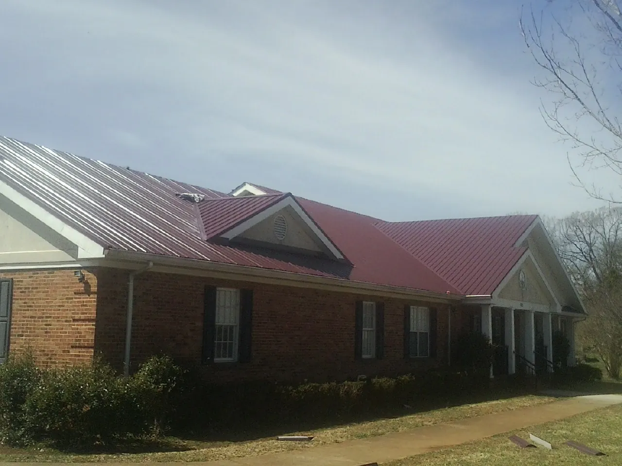 Red metal roof with gabled entries on a long brick building, from a Hail Damage Roof Repair job in Wake