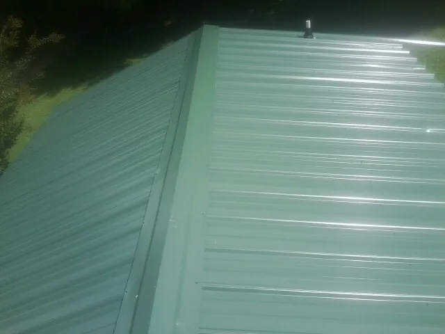 New green metal panels meeting at the ridge of a roof — Flat Roof Repair work by our crew in Wake