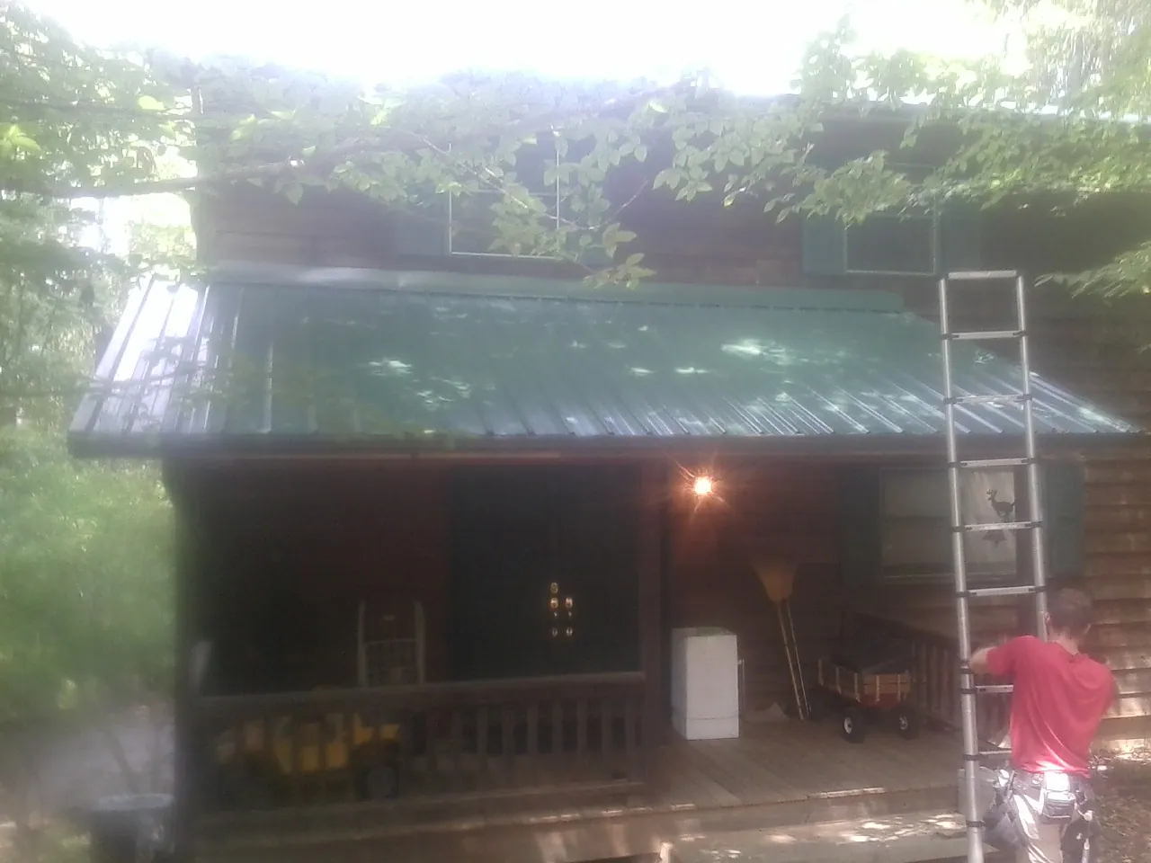 Worker on a ladder at the green porch roof of a wooded cabin in Wake
