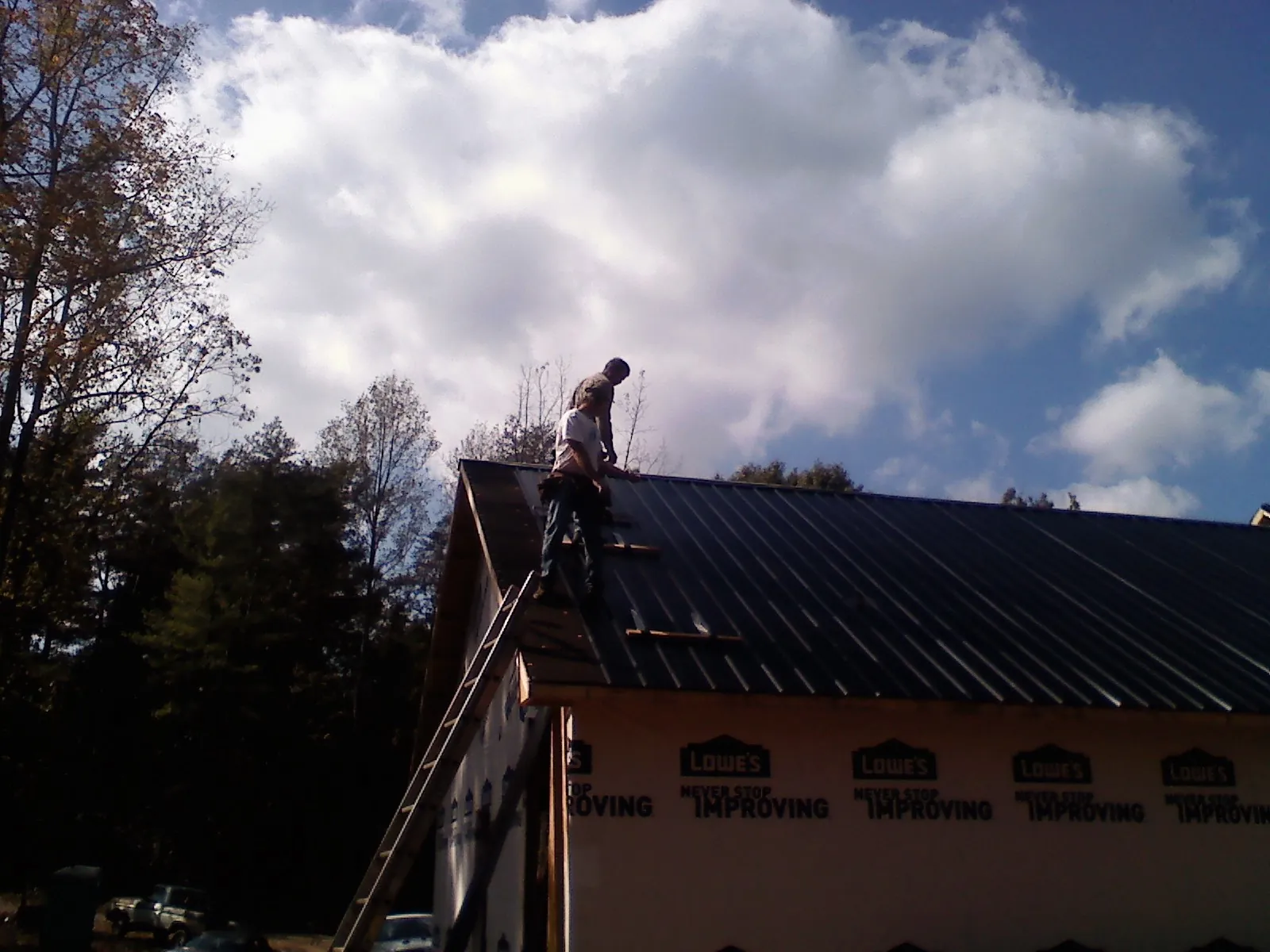 Roofer fastening dark metal panels high against a cloudy sky, from a Roof Inspection job in Wake